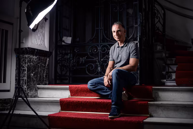 Mann sitzt auf roten Treppenstufen vor eleganter Hausfassade, professionelle Studiobeleuchtung, selbstbewusstes Portrait