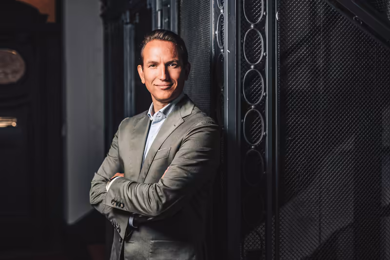 Mann in Businessanzug mit verschränkten Armen vor Serverrack, professionelles Porträt in IT-Umgebung