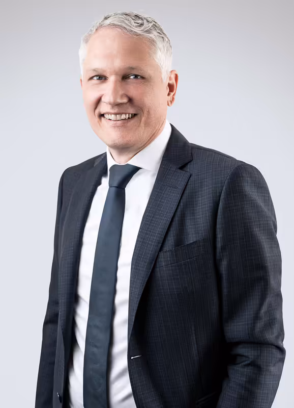 Geschäftsportrait Mann mittleren Alters in dunklem Anzug und Krawatte, lächelnd vor hellem Hintergrund
