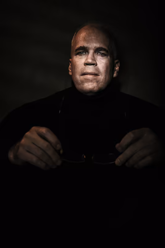 Mann in schwarzem Pullover, ernster Blick, dramatische Porträtbeleuchtung vor dunklem Hintergrund