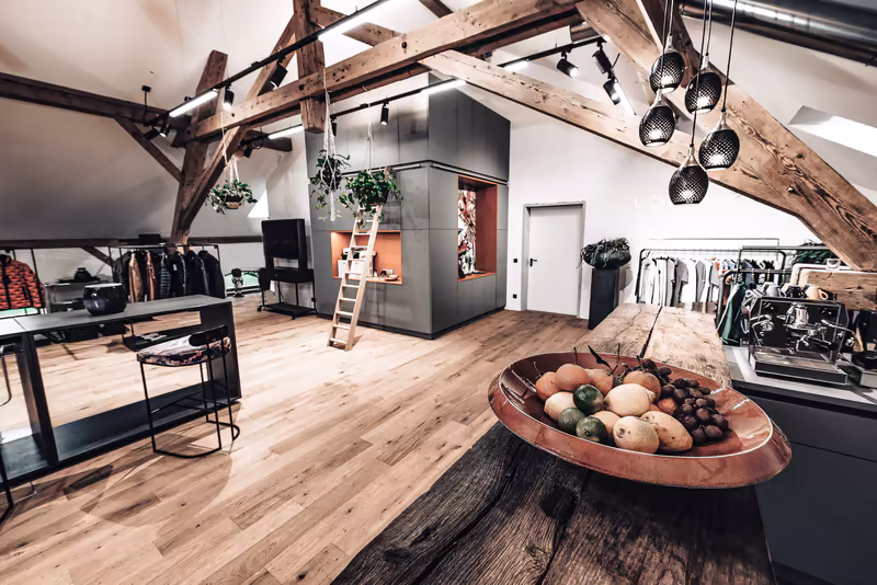 Modernes Loft-Büro mit Holzbalken, Arbeitsplatz, Kleidungsständern und Deko-Obstschale im Vordergrund