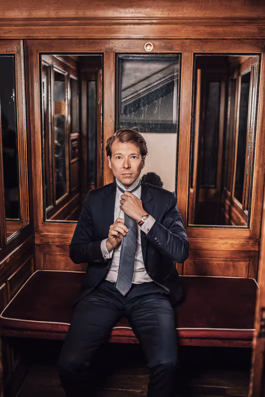 Geschäftsmann in dunklem Anzug bindet Krawatte in edlem Holzwagen, klassische Business-Porträtaufnahme