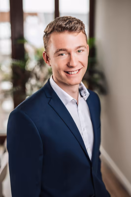Mann in dunklem Businessblazer und hellblauem Hemd lächelt in modernes Büro-Interieur mit Pflanzen, Porträtfotografie