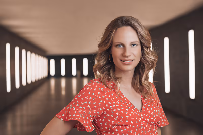Frau in rotem Blütenhemd lächelnd in moderner Flurarchitektur mit LED-Beleuchtung, Business-Portrait