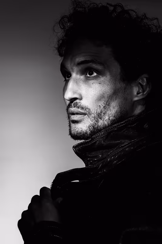 Mann mit lockigem Haar im Porträt-Profil, Schwarz-Weiß-Fotografie, ernster Blick, dunkle Jacke, minimalistischer Hintergrund