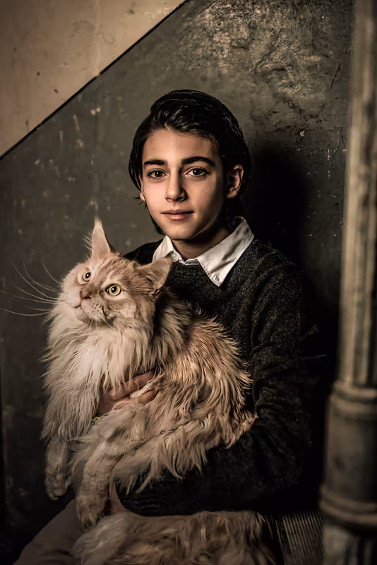 Junger Mann mit flauschiger Maine-Coon-Katze vor strukturierter Wand, Porträtfotografie mit warmem Licht