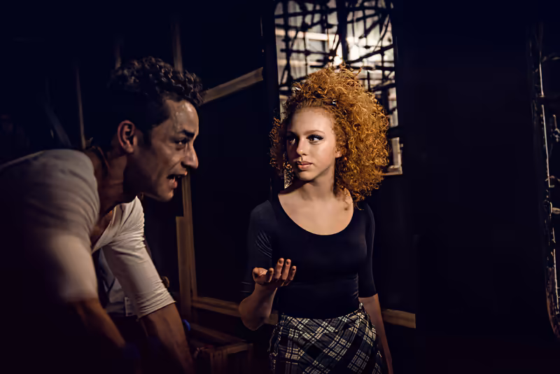 Zwei Personen im Gespräch, dramatische Beleuchtung, dunkles Studio-Setting mit geometrischen Strukturen im Hintergrund