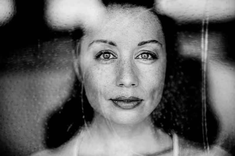 Schwarz-Weiß-Porträt einer Frau mit direktem Blick, unscharfer Hintergrund, ausdrucksstarke Augen und nachdenkliche Gesichtsausdruck
