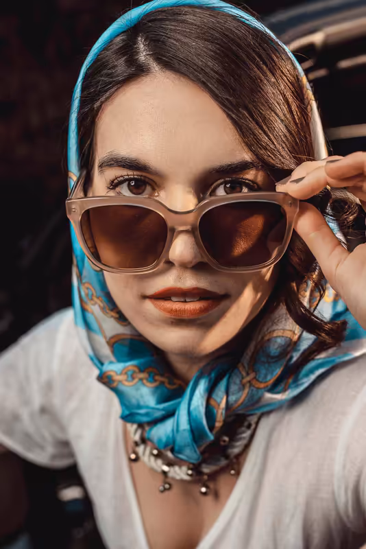 Frau mit türkisem Kopftuch und Sonnenbrille, blickt in Kamera, türkisfarbenes Neonlicht