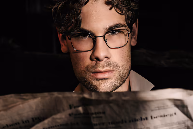 Mann mit Brille liest Zeitung, dramatische Beleuchtung vor dunklem Hintergrund