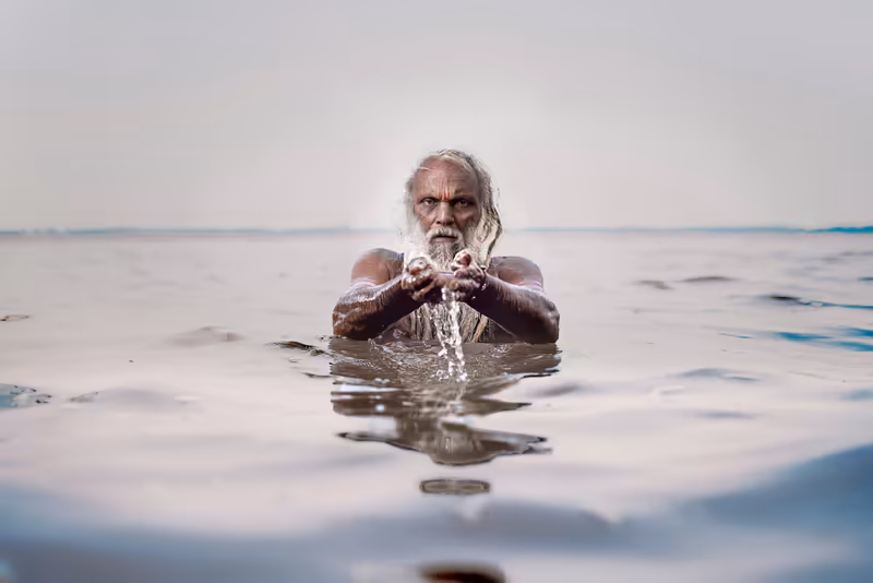 Älterer Mann mit weißem Bart badet im flachen Meerwasser und spritzt sich Wasser ins Gesicht, ruhige Stimmung