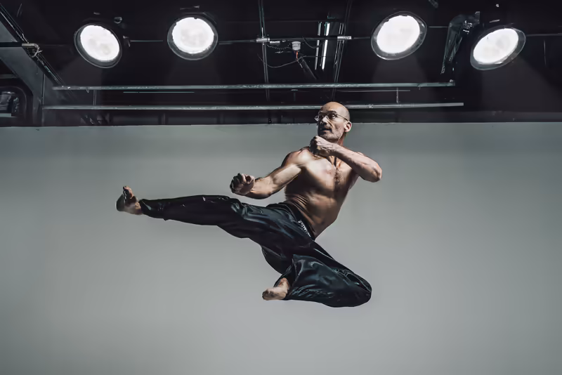 Mann in Kampfsportpose springend vor Studio-Hintergrund mit Profi-Beleuchtung