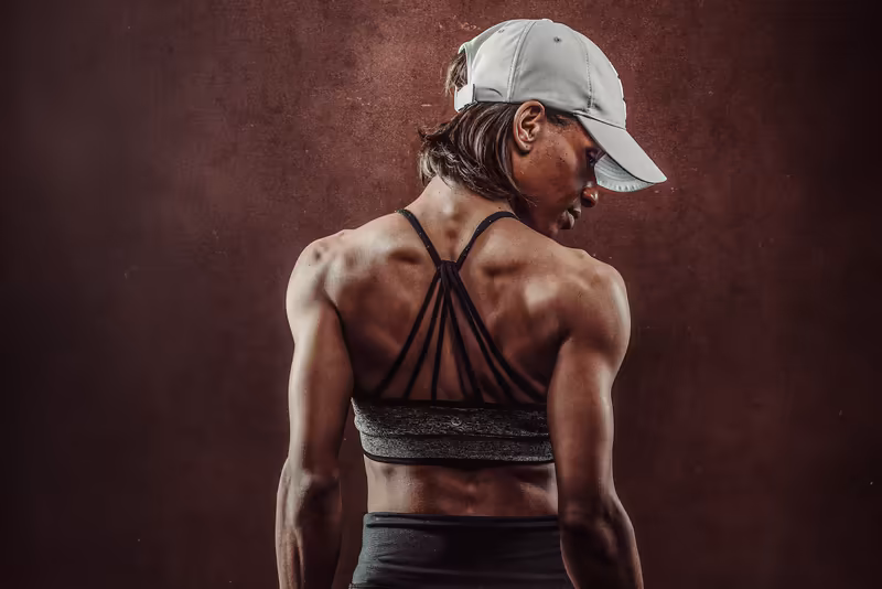 Athletische Frau von hinten in Sportoutfit und weißer Kappe vor bordeauxrotem Hintergrund