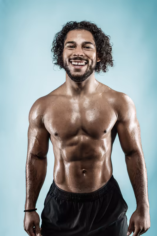 Muskulöser Mann mit lockigem Haar lächelt vor blauem Hintergrund, Porträt-Studio-Fotografie