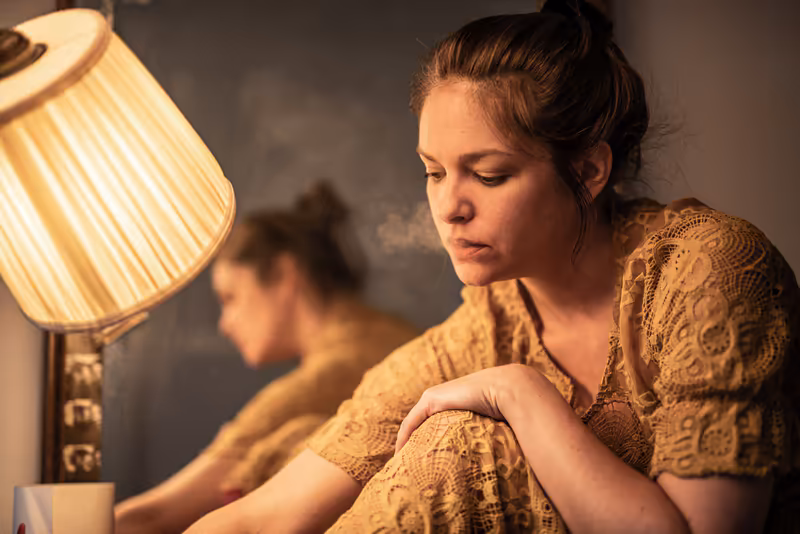 Frau sitzt nachdenklich unter Schreibtischlampe, warmes Licht, intime Atmosphäre